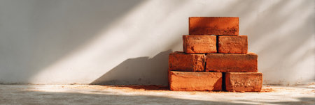 A vertical arrangement of red bricks sits against a concrete surface, creating shadows with a clean backdrop. Dust reflects sunlight in a serene atmosphere.の素材
