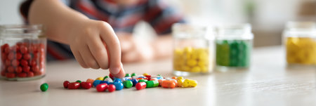 Young child eagerly extends hand to colorful candies scattered on counter with jars filled with sweets in the background, creating a playful atmosphere.の素材