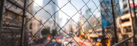 Scaffold and protective netting are installed over a busy urban street as pedestrians and vehicles navigate through the bustling scene under clear skies.の素材