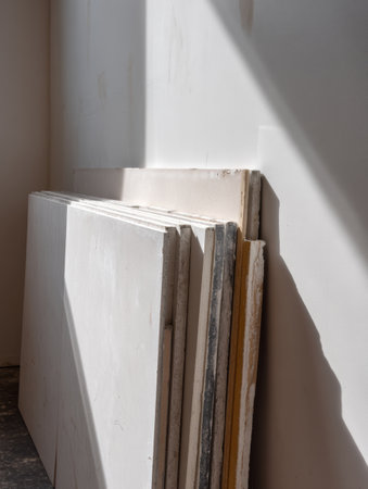 Drywall panels are stacked and leaning against a wall, showcasing their smooth surface and bright, clean appearance in this interior environment.の素材