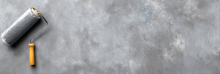 Paint can and roller are positioned neatly on a smooth concrete background, indicating preparation for a home renovation or painting task.の素材