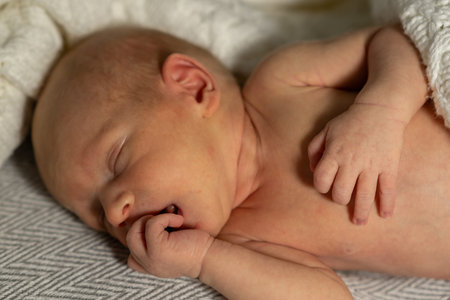 A newborn baby is peacefully sleeping, nestled in a soft blanket, with tiny hands tucked under chin,...