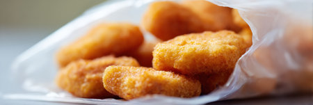 Frozen chicken nuggets are displayed in clear, crisp packaging showing their golden texture, ready to be prepared for a meal at home.の素材