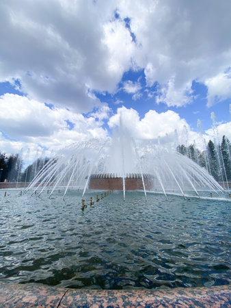 Water jets erupt from the fountain, creating a stunning display in the parks pond, surrounded by...