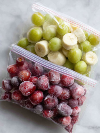 Frozen grapes and banana pieces are neatly packed in zip bags with the tops open, ready to be enjoyed as a nutritious snack or smoothie ingredient.の素材