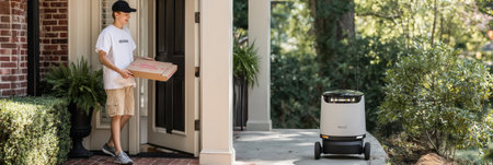 A teen stands at the doorway holding a frozen pizza box received from a delivery robot waiting on the right side of the pathway in a residential area.の素材