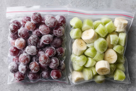 Frozen grapes and banana chunks are stored in open zip bags, showcasing convenient snack options or smoothie ingredients ready for use.の素材