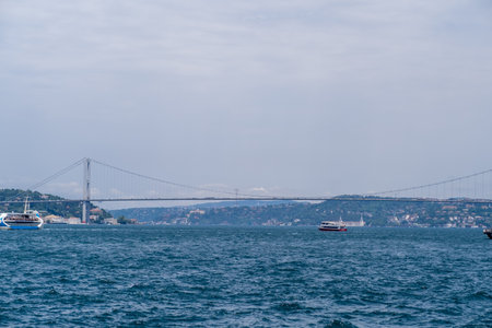 Ships navigate the waters of the Bosphorus, showcasing the impressive bridge that links the two shores against a serene blue sky.の写真素材