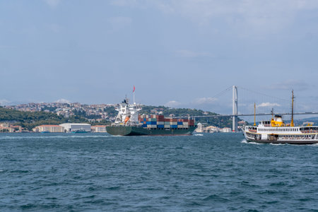 Cargo ships navigate the Bosphorus strait while a ferry crosses the water, with the city skyline visible in the background under clear skies.の写真素材