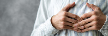 Hands create a heart shape over the chest, symbolizing warmth and compassion in a healthcare context. The background is gray, enhancing focus on the gesture.の素材