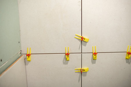 Workers are using yellow tile leveling clips secured with rubber rings to ensure even tile placement on a wall in a home renovation setting.の写真素材