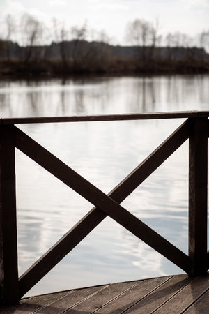 A wooden railing creates a frame for tranquil water reflecting the soft light of early morning, with trees lining the banks in the distance.の写真素材