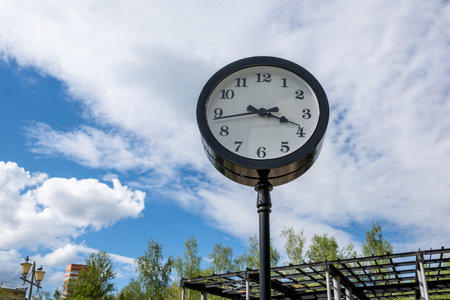 A decorative clock stands tall in a park surrounded by greenery, displaying the time around three oclock on a sunny afternoon.の写真素材