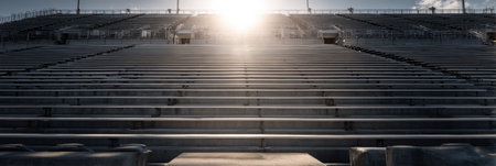 Bleachers stand empty in a stadium, highlighted by a bright sunbeam shining through, with clear upper space reflecting a tranquil pre-game moment.の素材