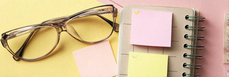 Planner open with vision care reminder written in pastel colors, featuring stylish glasses, adding to a neat, organized workspace setting.の素材