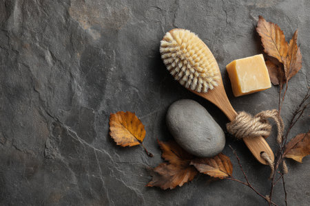 A massage brush made of natural materials sits beside a bar of soap and dry leaves on a stone surface, evoking a serene ambiance perfect for relaxation.の素材