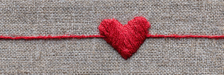A red thread forms a heart shape on a natural linen surface, illustrating skillful embroidery. The blank space above highlights the handmade artistry.の素材