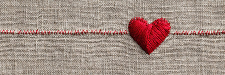 Heart shape made from red thread is stitched onto a neutral linen background, showing the craftsmanship and creativity involved in textile art.の素材