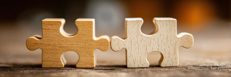 Two wooden puzzle pieces fit together on a rustic background, symbolizing teamwork, unity, and collaboration in a professional or personal context.の素材