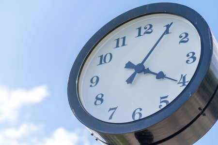 Classic clock shows a time of four oclock amid a bright blue sky and fluffy clouds, situated in a...