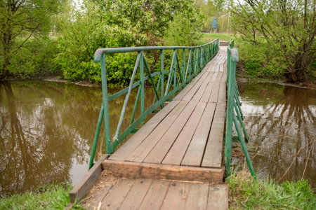 Wooden Bridge Over a Peaceful Stream Surrounded by Greenery in a Serene Countryside Setting During Springtimeの写真素材