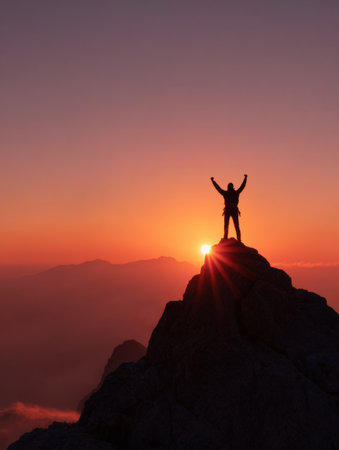 A climber stands triumphantly at the summit, silhouetted against a vibrant sunrise. The scene captures the beauty of nature and the spirit of adventure.の素材