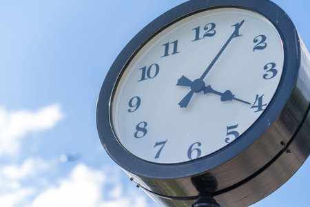 Large clock mounted on a post displays the time shortly before four oclock with a vibrant blue sky...