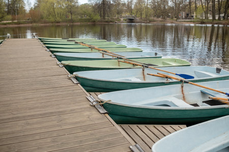 Calm lake reflects surrounding greenery while rowboats rest on a dock, inviting visitors for a tranquil paddle on a sunny spring day.の写真素材