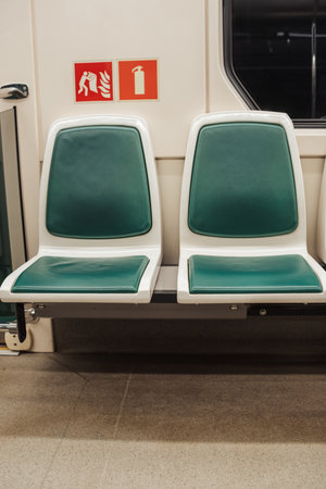 Two empty green and white seats are positioned side by side in a subway train during nighttime, highlighting urban transit design and functionality.の写真素材