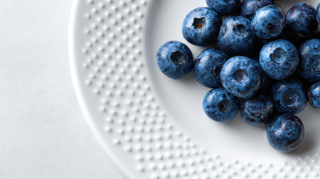 Plump blueberries rest on a textured white ceramic plate, emphasizing their rich color and freshness while leaving a clean space on the right margin.の素材