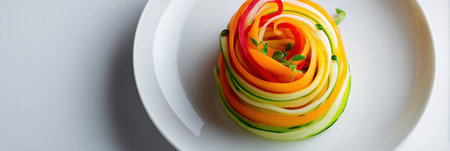 A vibrant spiral of fresh vegetables rests on a pristine white plate, emphasizing simplicity and modern presentation in a bright, inviting setting.の素材