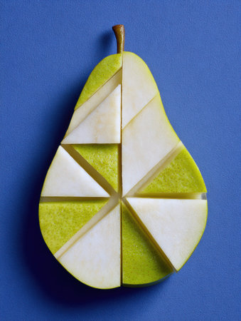 Bright green pear slice segmented into distinct geometric shapes displayed on a smooth blue surface, highlighting the fruits vibrant colors and patterns.の素材