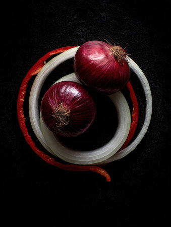 Red onions and pepper form floating rings against a black surface, showcasing their vibrant colors and minimalist arrangement in an artistic culinary displayの素材