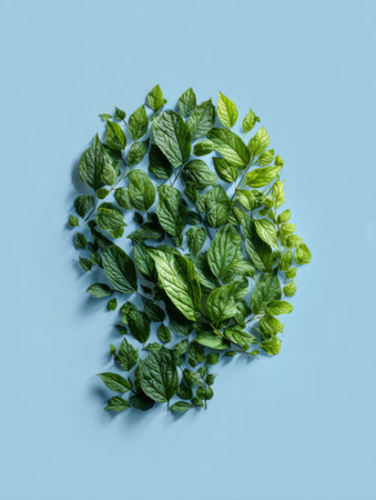 Calming green leaves are meticulously arranged to create a human head silhouette on a soft blue background, symbolizing nature and tranquility.の素材