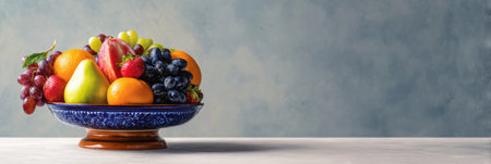 Fruit bowl features a variety of fresh, vibrant fruits arranged artistically on a decorative base, set against a smooth, contemporary background.の素材