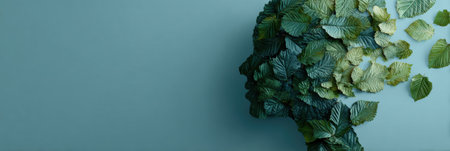 A silhouette of a human head composed of calming green leaves is set against a tranquil blue backdrop, creating a serene and natural atmosphere.の素材