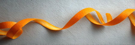 A vibrant orange zest ribbon swirls elegantly over a matte surface, adding a bright touch to the simple design above.の素材
