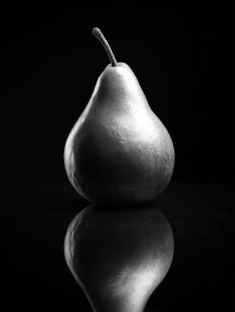 A solitary pear creates a striking visual against polished black glass, highlighted by dramatic lighting that enhances its smooth surface and shape.の素材