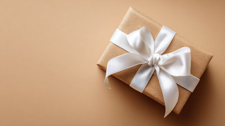 A beautifully wrapped gift featuring a white ribbon is positioned elegantly on a soft tan background, ideal for conveying a celebratory mood and excitement.の素材