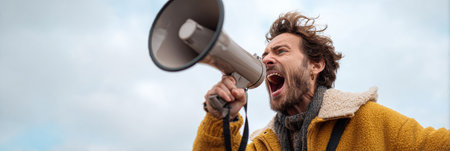 A demonstrator is shouting into a megaphone, advocating for freedom of speech during an outdoor rally, surrounded by an engaged crowd.の素材