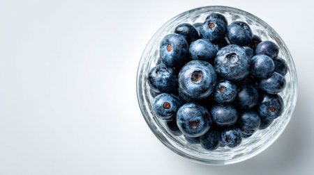 A bowl filled with ripe blueberries rests on a white surface, showing their deep blue color and round shape against a bright background.の素材