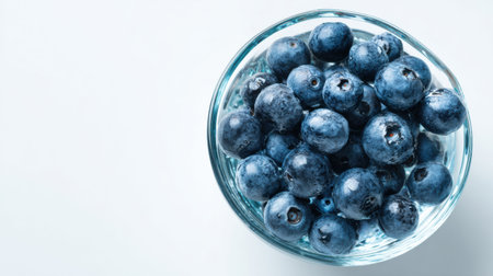 Fresh blueberries are elegantly arranged in a clear glass bowl, creating a simple yet captivating still life against a pristine white backdrop.の素材