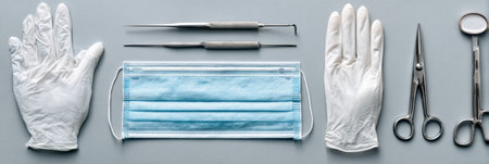 Neatly arranged surgical mask, gloves, and instruments are displayed on a clean surface, creating an organized setup for a medical procedure.の素材