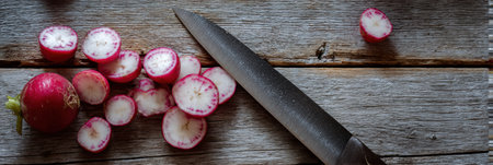 Freshly sliced radishes are arranged on a weathered wooden surface alongside a knife, perfect for meal preparation in a kitchen setting.の素材
