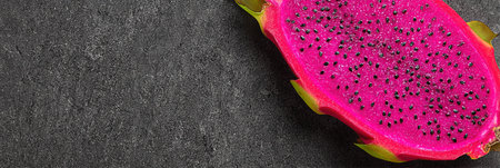 A vibrant slice of neon pink dragon fruit rests on a textured charcoal background, showing its unique color and appearance with plenty of empty space nearby.の素材
