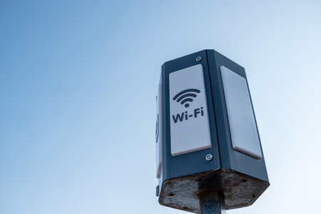 A metal pole supports a public Wi-Fi hotspot with clear symbols against a blue sky, offering...
