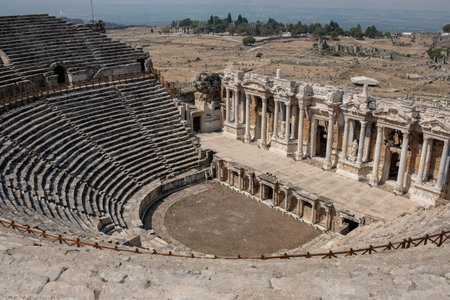 Visitors admire the breathtaking ancient amphitheater in Pamukkale, surrounded by remnants of historic buildings and scenic landscapes.の写真素材