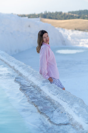 A young woman poses by the beautiful travertine pools of Pamukkale, soaking in the warm sunlight and breathtaking landscape on a clear day.の写真素材