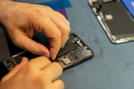 Technician focuses on repairing a smartphone, carefully handling internal components in a neat,...