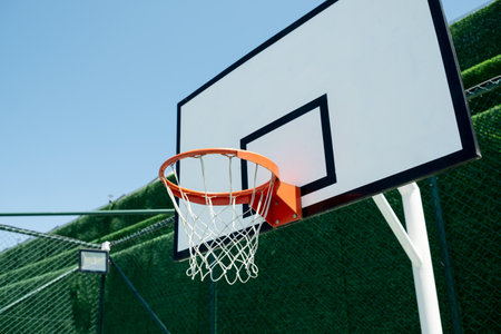 Brightly colored basketball hoop stands on an outdoor court, surrounded by green fencing and a clear...
